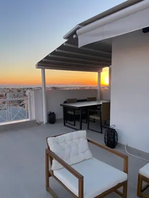 a white chair and a table on a balcony with the sunset at Glyf Seaview Penthouse by Taurus in Athens