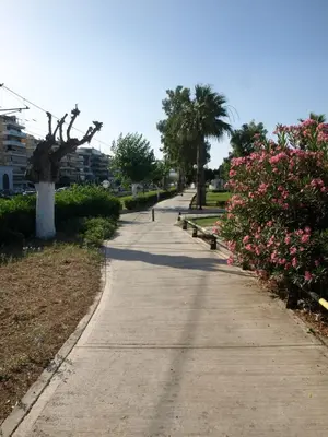 a sidewalk in a park with pink flowers and trees at Alimos Kalamaki 100 meters from the Beach in Athens
