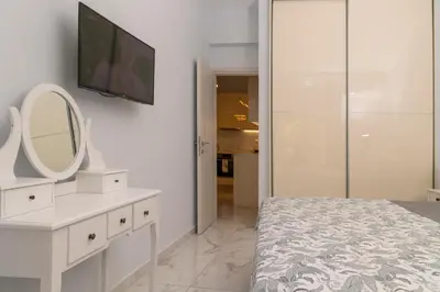 a white bedroom with a mirror and a tv on the wall at Simpli-city home in Piraeus