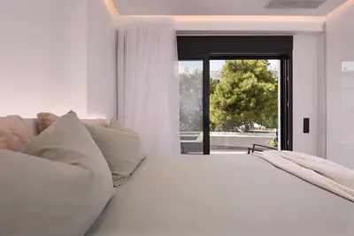 a white bedroom with a large bed and a window at Emerald Stone Apartment Varkiza in Vari