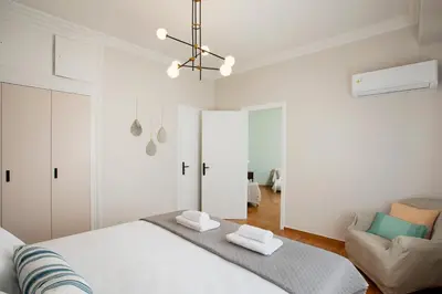 a white bedroom with a bed and a chair at Hospes - Chic retro retreat in the heart of Athens in Athens