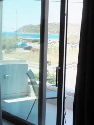 a window with a chair looking out at a beach at Golden Sand Suites in Anavissos