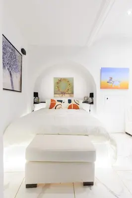 a white bedroom with a white bed with an ottoman at Aiolos luxury apartment under acropolis in plaka in Athens