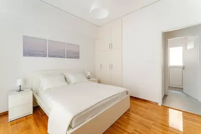a white bedroom with a large white bed and wooden floors at George's Cozy 60m2 Apartment 7' Metro in Athens