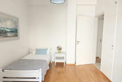 a white bedroom with a bed and a table at Ήσυχο φωτεινό δωμάτιο με βεράντα in Athens
