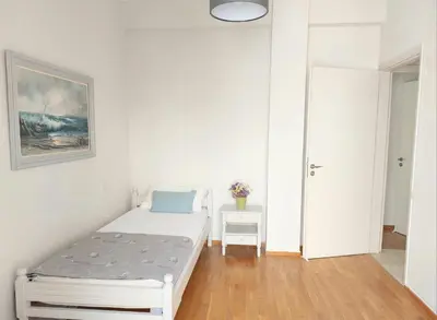 a white bedroom with a bed and a table at Ήσυχο φωτεινό δωμάτιο με βεράντα in Athens