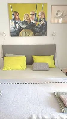 a bed with yellow pillows and a painting on the wall at quiet apartment near the sea in Athens