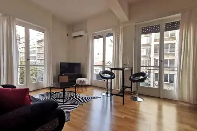 a living room with two chairs and a television and windows at CDV stylish Athens flat in Athens
