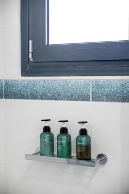 a shelf with three bottles of shampoo and a mirror at Indoor pool villa, near the beach, Lagonisi in Kalívia Thorikoú
