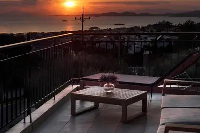 a table on a balcony with a sunset in the background at Thenia's Bellevue apartment in Saronida