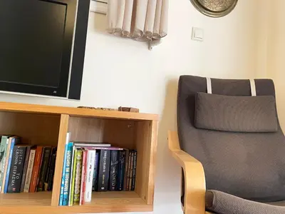 a tv sitting on top of a book shelf next to a chair at Saronida Beach Nest Apartment in Saronida