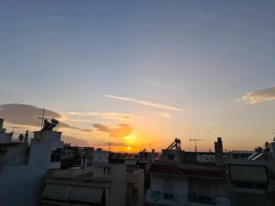 a sunset over the roofs of buildings in a city at ''Athens Light'' luxury spacy appartment, Agia Paraskevi in Athens