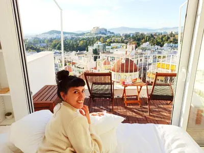a woman sitting on a bed on a balcony at Rooftop studio with Acropolis view just next to Panathenaic Stadium - 280 Athens view in Athens