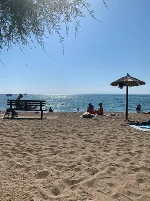 a group of people sitting on a beach with an umbrella at Renovated fully equipped 2 Bedroom cozy Apartment near the sea in Athens