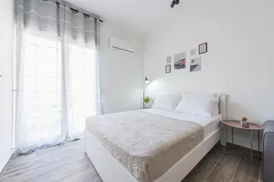 a white bedroom with a bed and a window at Kallithea Kyprou Square ! in Athens
