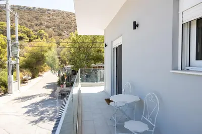 a white house with a balcony with a table and chairs at The Pines apartment in Palaiá Fókaia