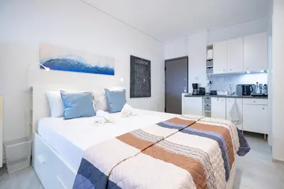 a white bedroom with a large bed and a kitchen at Stylish studio for 2 in Abelokipi by MPS in Athens
