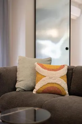 a pillow on a brown couch with a table at LIV - Peaceful Pagrati Getaway in Athens