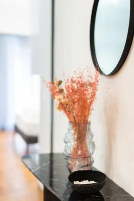 a vase with flowers on a table with a mirror at LIV - Peaceful Pagrati Getaway in Athens