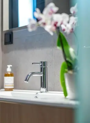 a bathroom sink with a green vase with a flower at The Meta Stay - Rooftop Access Downtown Studio in Athens
