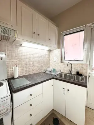 a kitchen with white cabinets and a sink and a window at Sea the City - Chic 2-BDR Escape with Spacious Living in Athens