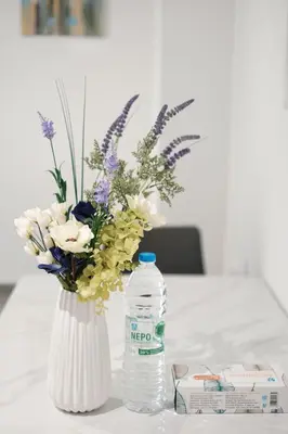 a white vase with flowers and a bottle of water at Cozy Home With Cooking Near Tram in Piraeus