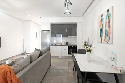 a living room with a couch and a table and a kitchen at Cozy Home With Cooking Near Tram in Piraeus