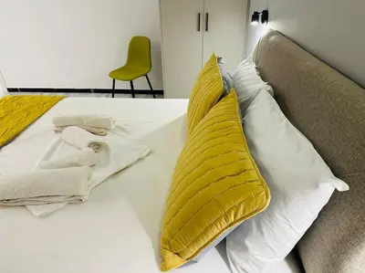 a white bed with a yellow pillow and a chair at Grey Suite at Piraeus Port in Piraeus
