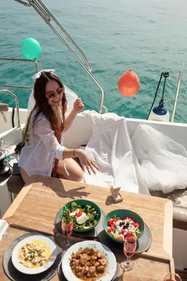 a girl sitting on a boat with plates of food at Luxury Sailing Cruises in Athens with Traditional Greek Cuisine and Drinks in Athens