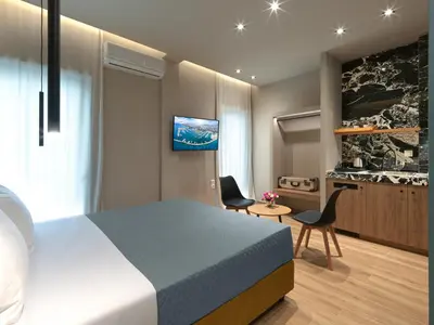 a bedroom with a bed and two chairs and a tv at YaPe Coastal Suites at Alimos Beach in Athens