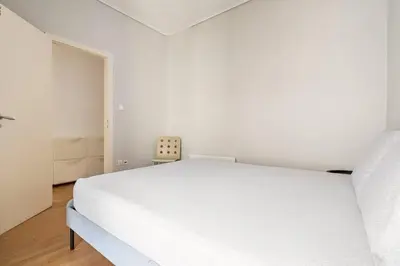 a white bedroom with a white bed and a chair at Sunny southern Athens flat near the seaside in Athens