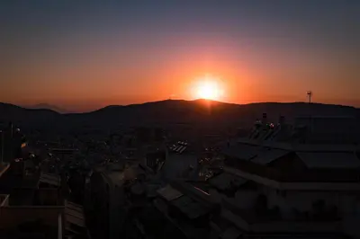 a sunset over a city with the sun setting on a mountain at Chic penthouse with stunning view in Athens