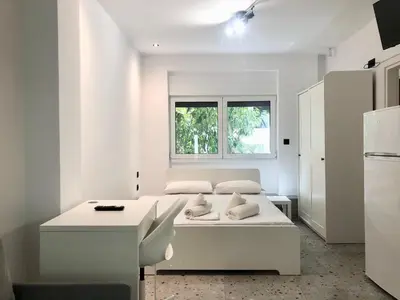 a white bedroom with a bed and a window at AIOLOS Pagrati Athens Hilton near METRO station in Athens