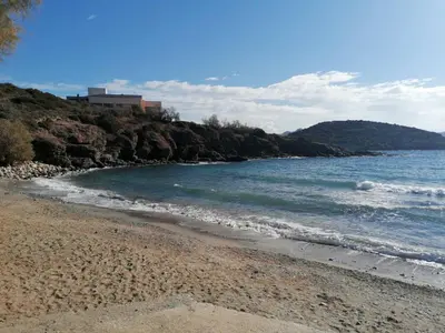 a beach with a building on a hill next to the water at Sea View Serenity in Athens in Anavissos