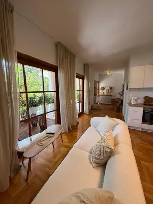 a living room with a white couch and a kitchen at The Gardenian - 15 min from Athens Airport in Paianía