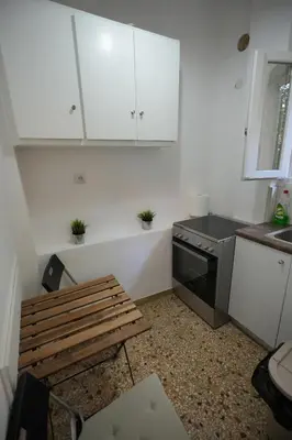 a kitchen with white cabinets and a bench and a stove at The Cozy Studio, Nea Smyrni in Athens