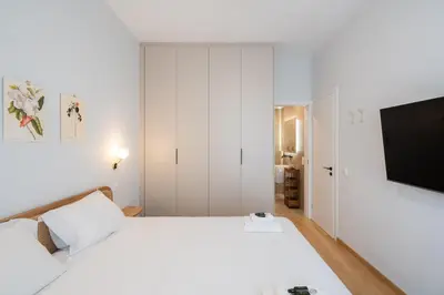 a bedroom with a white bed and a flat screen tv at 3BR Petralona Escape in Athens