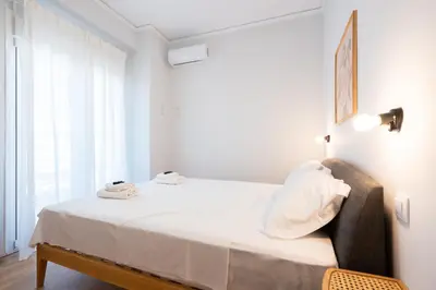 a bedroom with a bed with white sheets and a chair at 3BR Petralona Escape in Athens