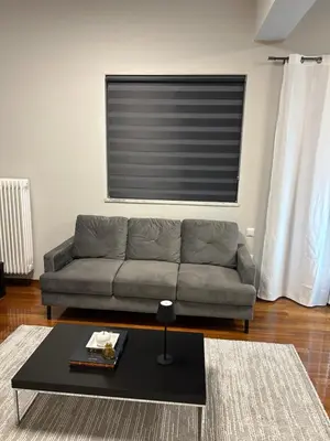 a living room with a grey couch and a window at comfort in Athens