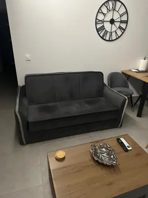 a black couch in a living room with a table and a clock at Elaion guest house in Athens
