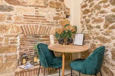 a table with green chairs in front of a stone wall at DP Homes Exarcheia 1B in Athens