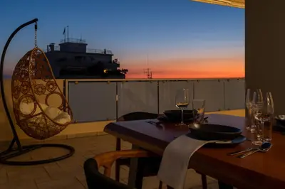 a table with wine glasses on a balcony with the sunset at Elegant Skyline Penthouse Acropolis View 3BR 2BA in Athens