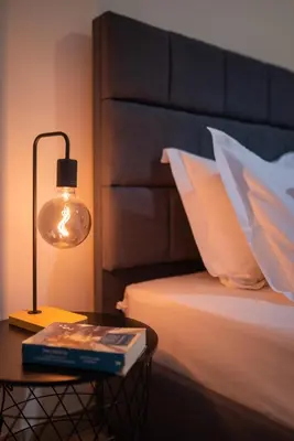 a lamp and a book on a table next to a bed at Central 2 Bdrm Aprt In Koukaki! in Athens