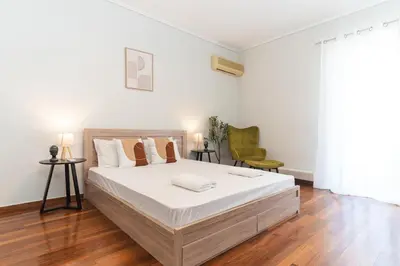a white bedroom with a large bed and a chair at Modern Seaside 2BR APT in Athens