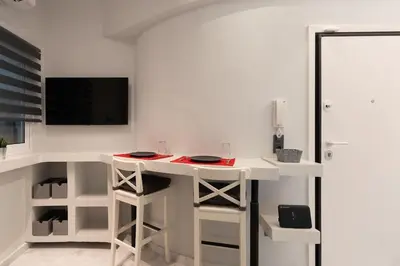 a white kitchen with a desk with a tv and stool at Unique Urban Gem in Neapoli Exarcheia in Athens