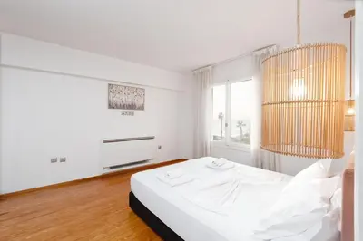 a white bedroom with a bed and a window at Zeus2 Beach Front Apartment, 3BR in Athens
