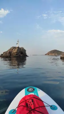 a surfboard in the water with a lighthouse in the background at Apartment next to the sea in Anavissos