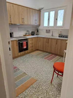 a kitchen with wooden cabinets and a red chair in it at Cozy apartment in Pagkrati in Athens