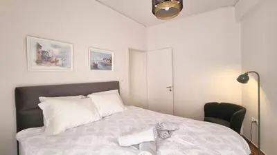 a white bedroom with a bed and a chair at Mata's Athenian Mosaic - super central city stay in Athens
