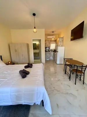 a bedroom with a large white bed and a kitchen at Ivory Escape Apartment - ATH Airport in Spáta